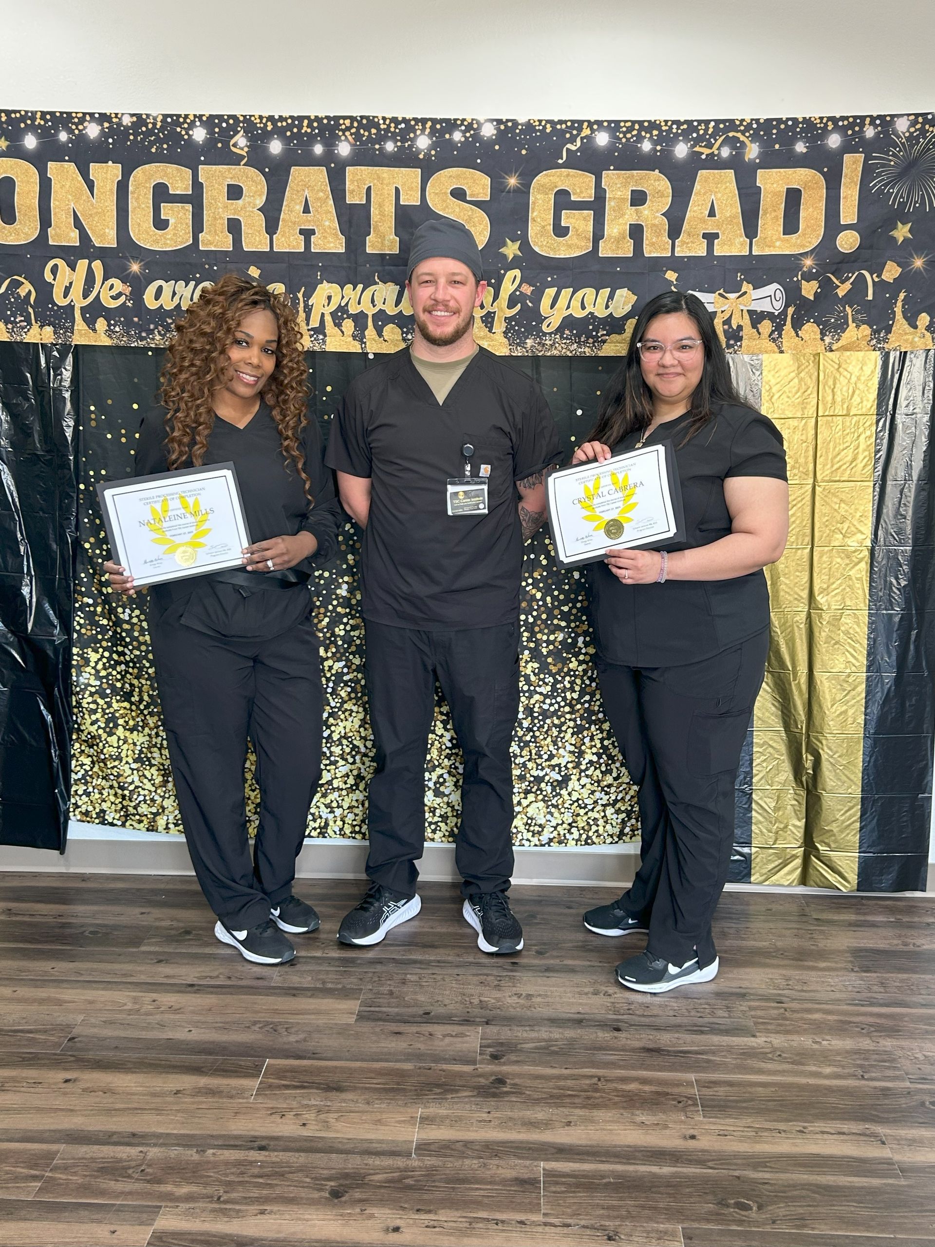 A man and two women are standing next to each other in front of a sign that says `` congrats grad ! ''