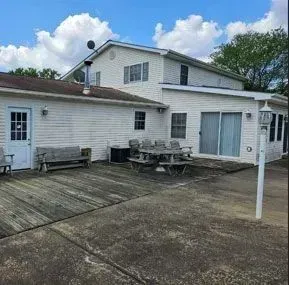White house with a wooden deck, concrete patio, and outdoor dining set, under a cloudy blue sky.