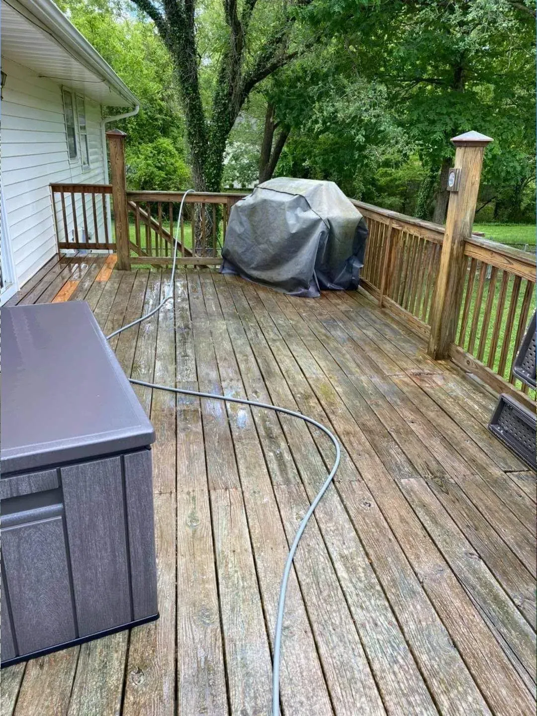 Wooden deck with a hot tub and grill; a hose is on the deck, and trees are in the background.