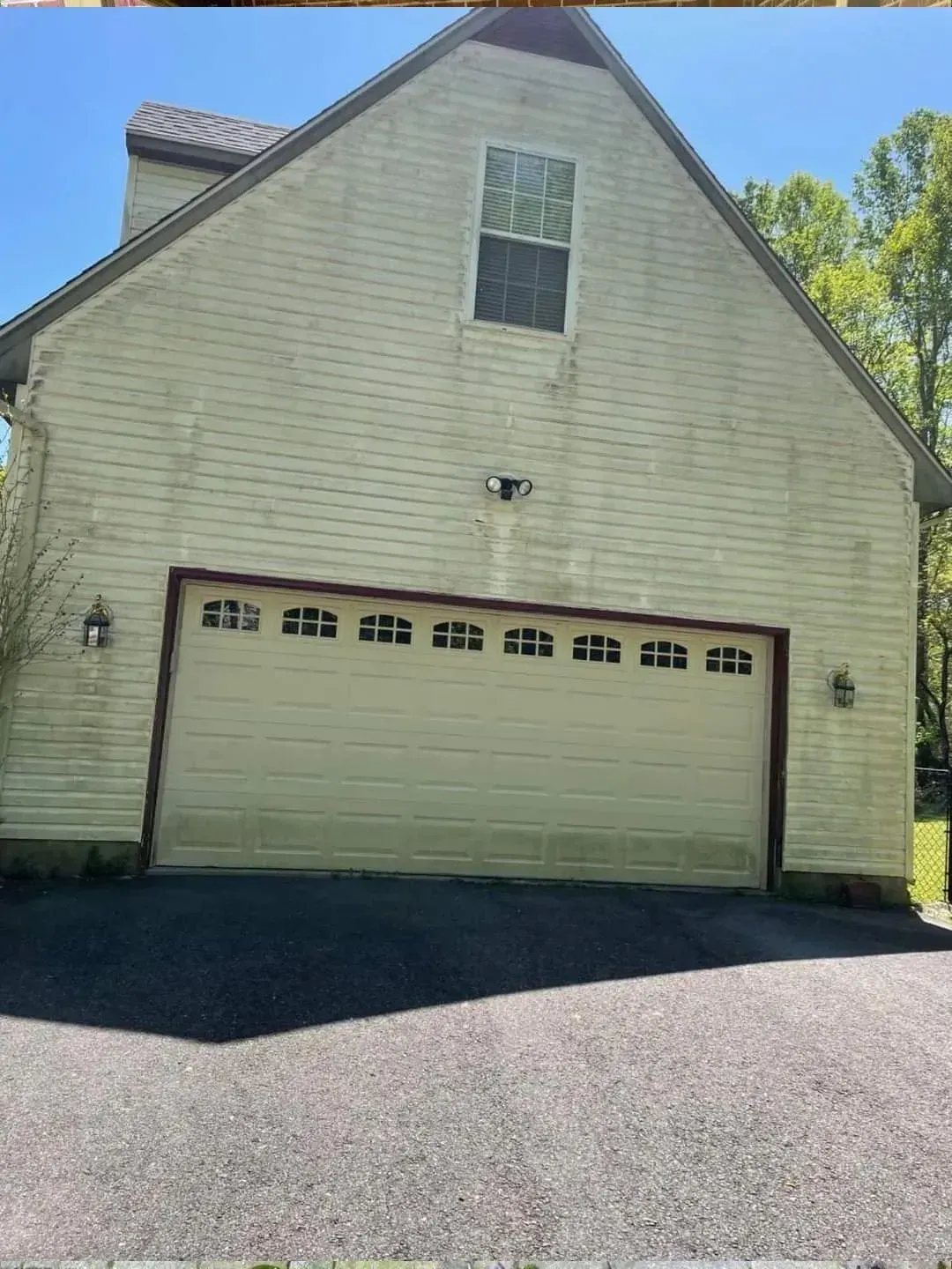 Yellow-sided house with a garage door and single window on top. Asphalt driveway.