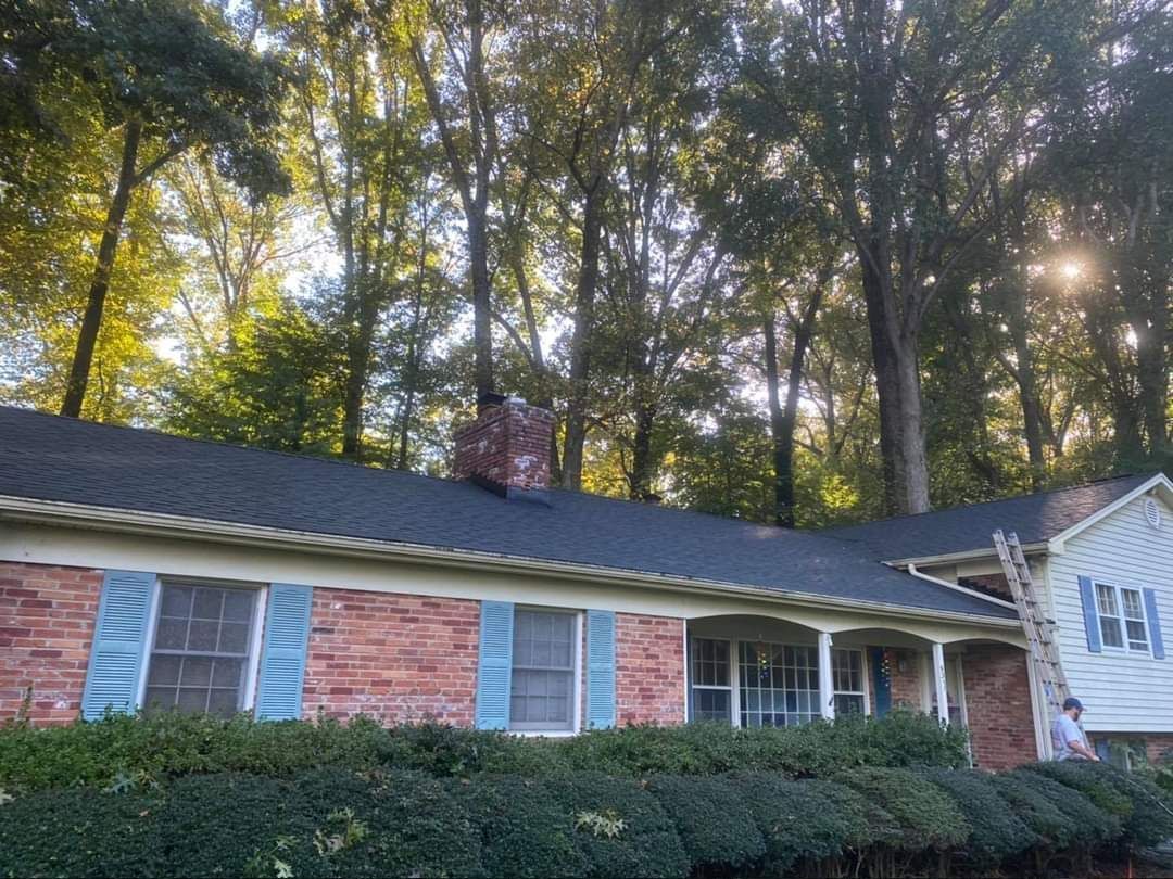 Brick house with a dark roof, chimney, blue shutters, and a ladder leaning against the side.
