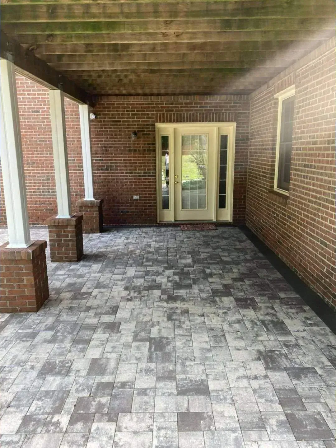 Brick patio with brick columns, walls, and a glass door. Grey pavers cover the floor.