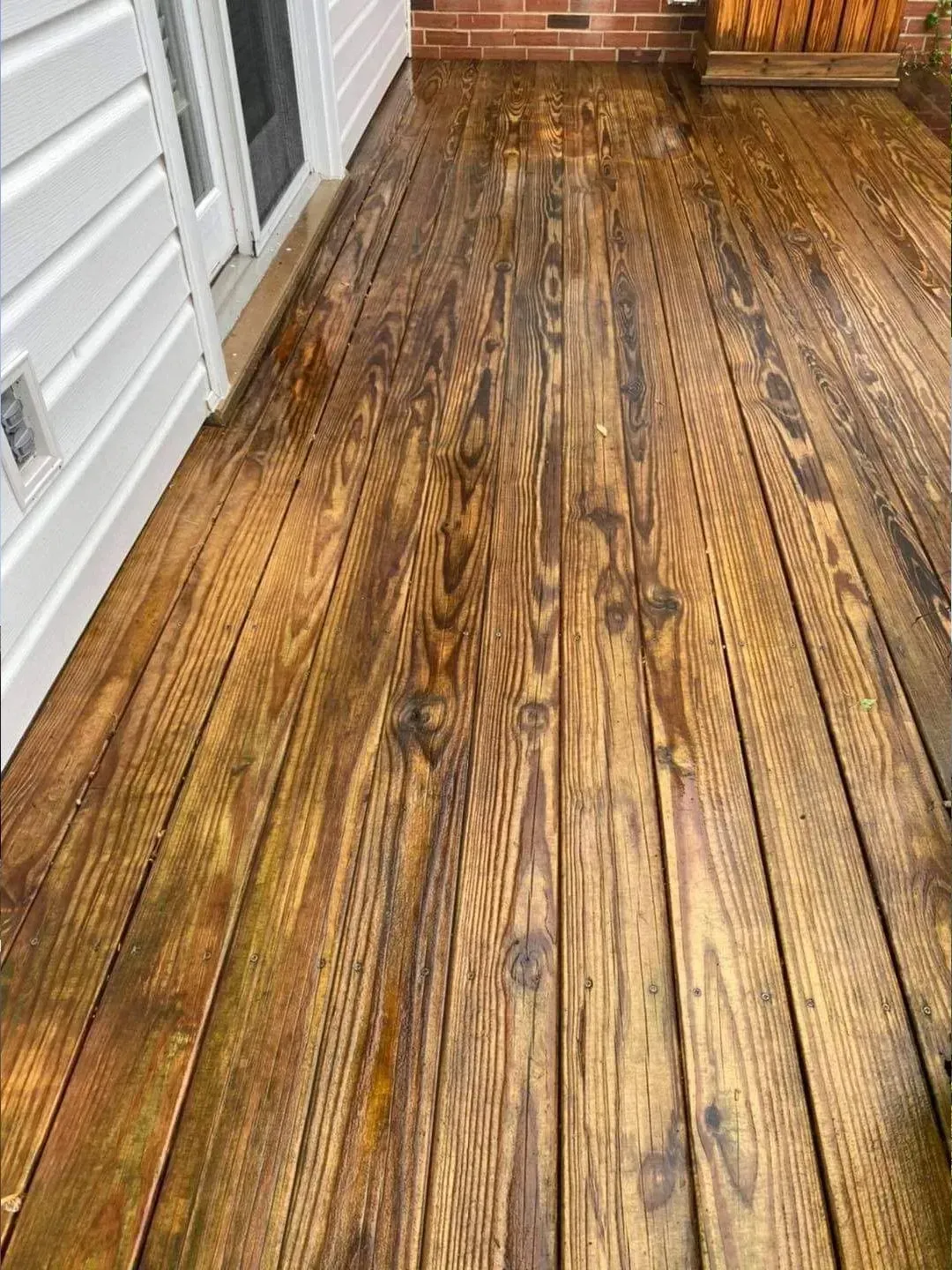 Wooden deck with aged stain, next to a white house wall.