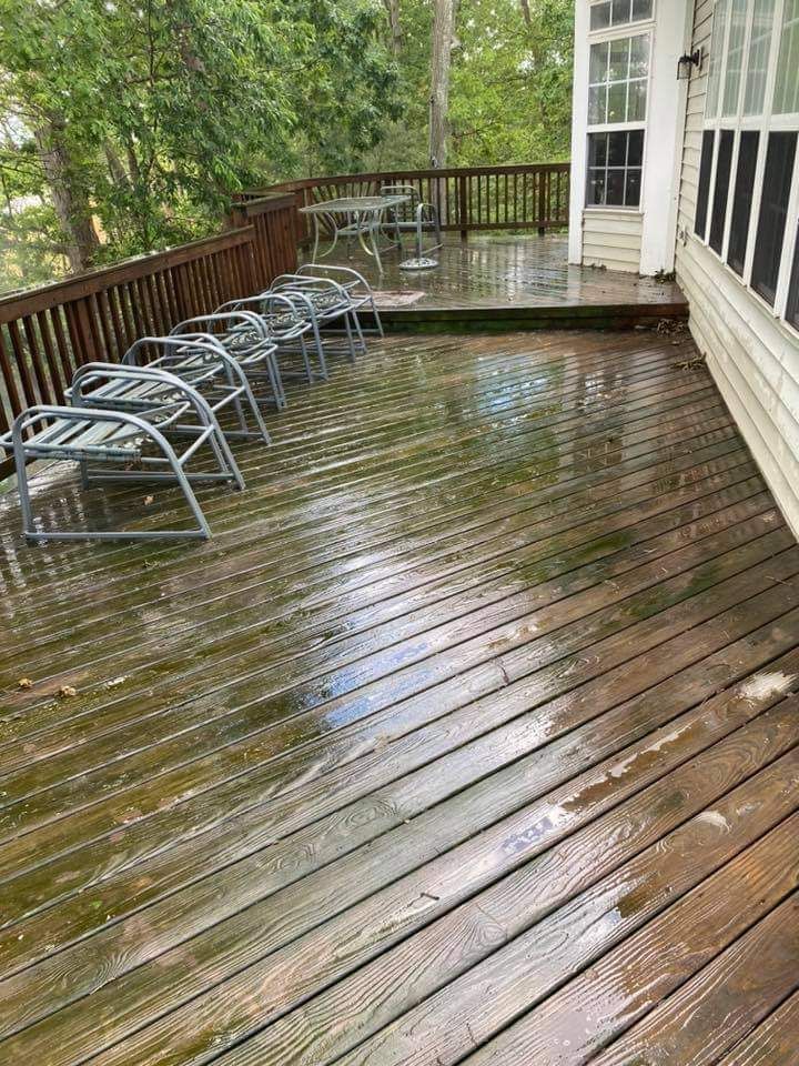 Wet wooden deck with several metal chairs. Back deck of a house with trees in the background.