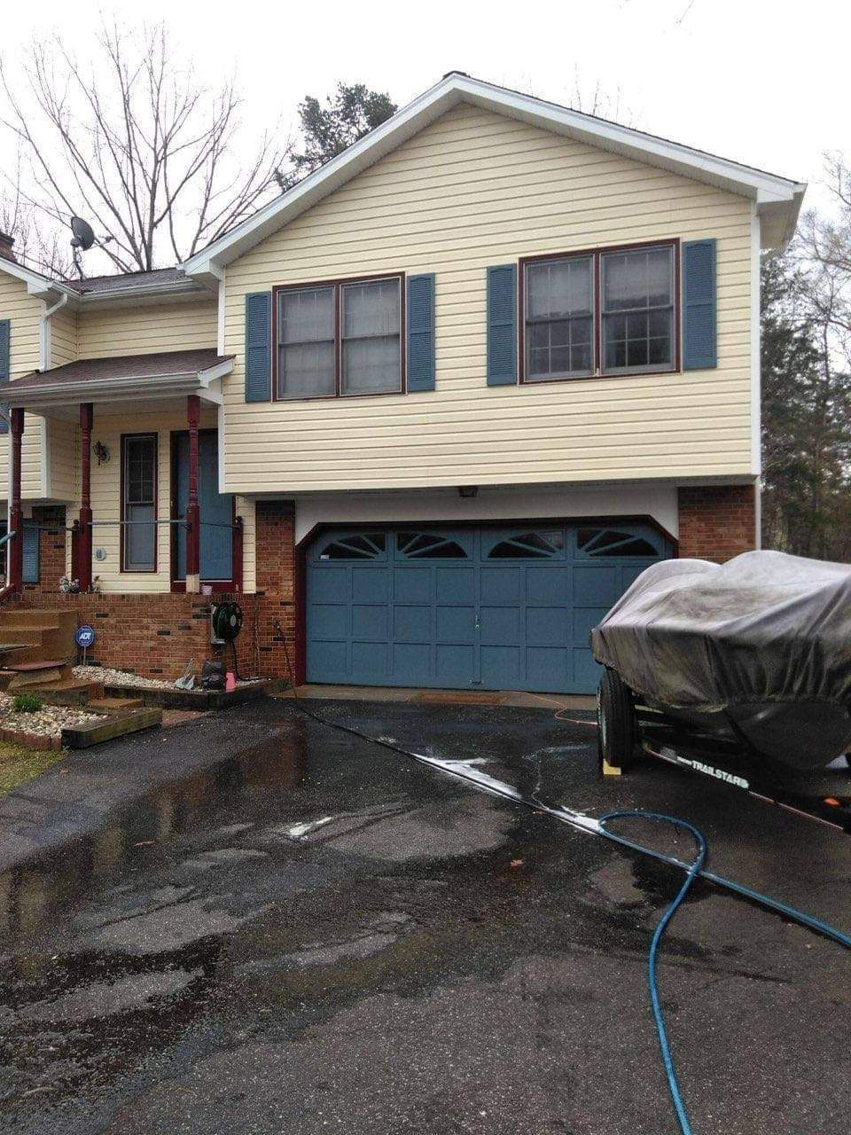 Two-story beige house with blue shutters and garage door; driveway with boat on trailer.