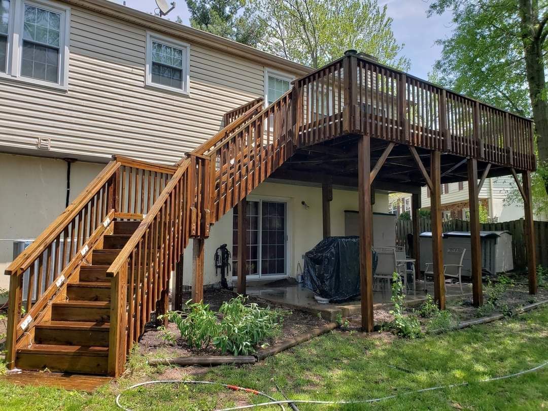 Wooden deck attached to a two-story beige house with stairs. Backyard setting with some patio furniture.