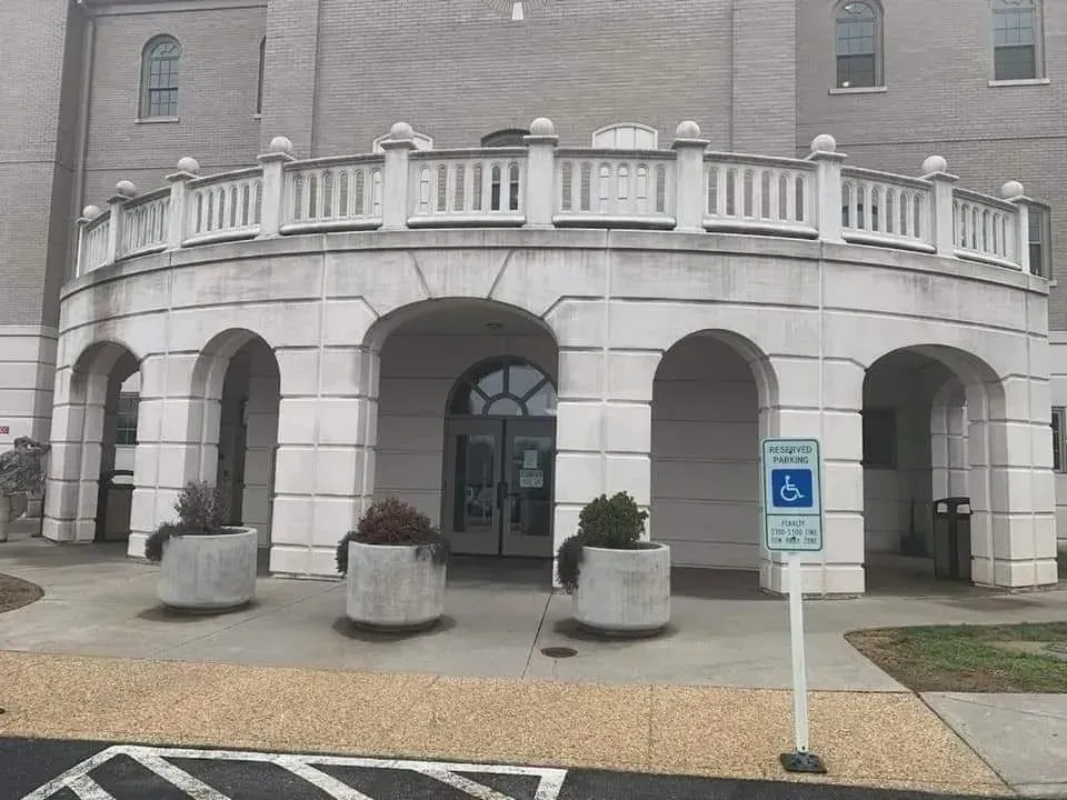 Entrance to a light-colored stone building with arched openings and a wheelchair accessible parking sign.