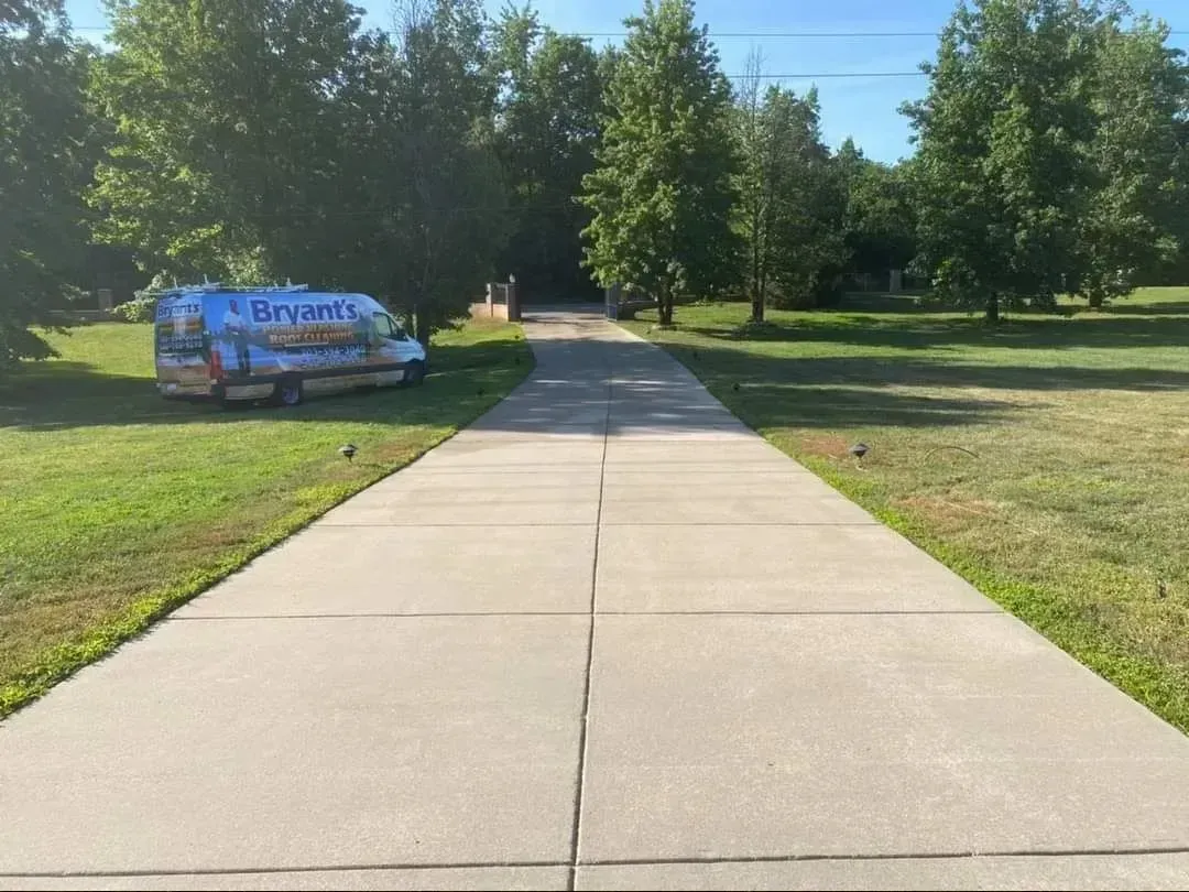 Concrete driveway leading to trees, Bryant's van parked on the left, sunny day.
