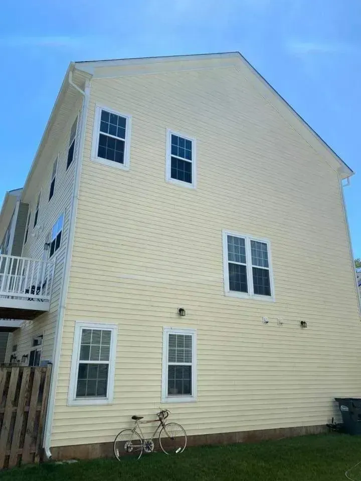Yellow-sided building with several windows, a bicycle, and a trash can against a blue sky.