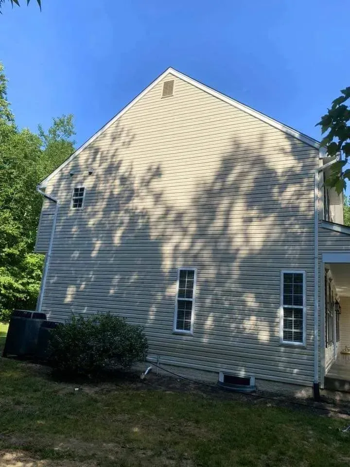 Side view of a two-story beige house with white trim and windows, in front of a blue sky.