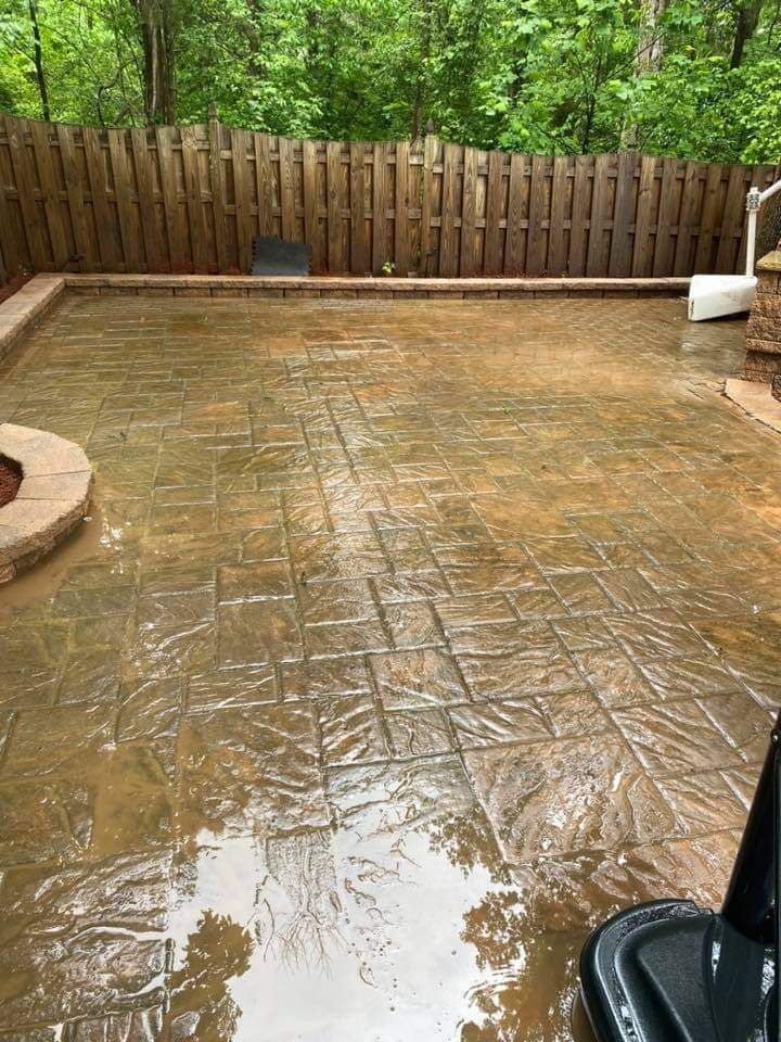 Wet stamped concrete patio with surrounding brick and wooden fence.