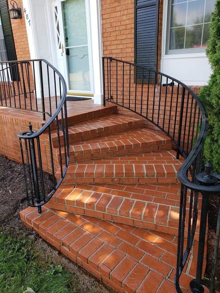 Brick steps with black wrought iron railing leading up to a white door.