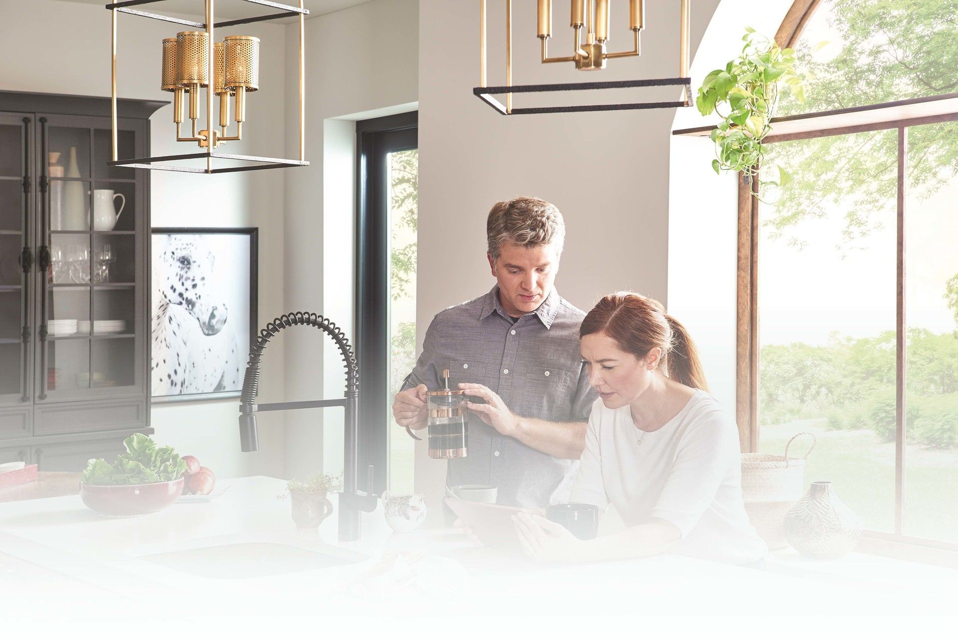 A man and a woman are looking at a tablet in a kitchen.