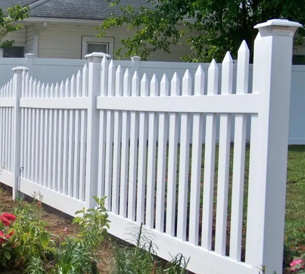 White picket fence in front of a white house with black shutters, on a green lawn.