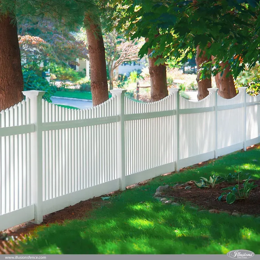 White picket fence in a green yard with trees, a house in the background on a sunny day.