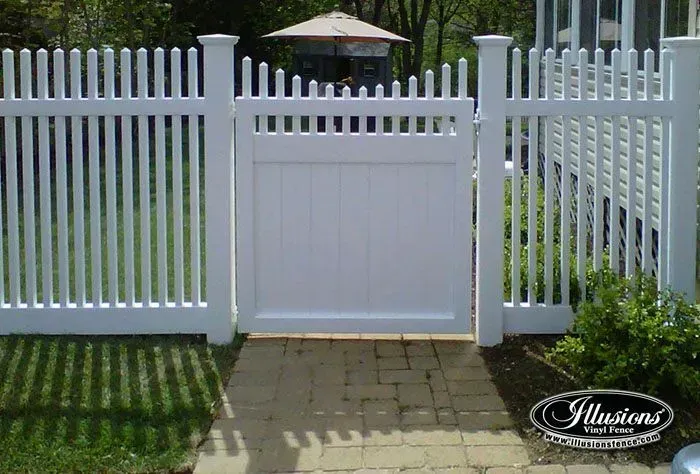 White picket fence with a solid panel gate, opening onto a brick pathway.