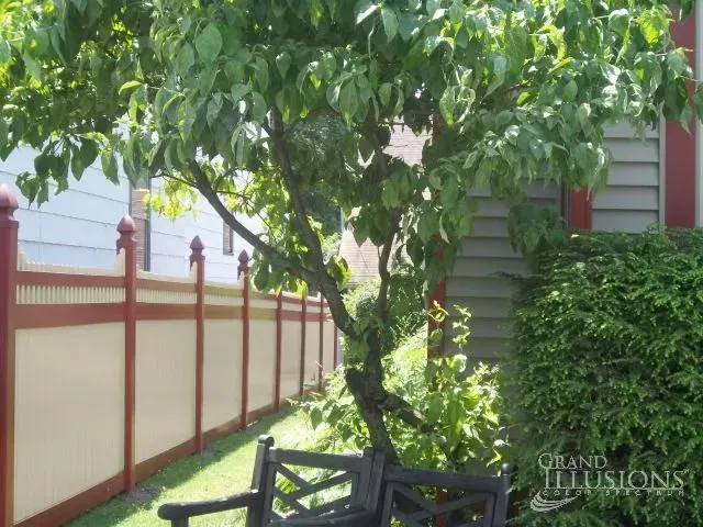 Tree and bench in a yard with a red and white fence.