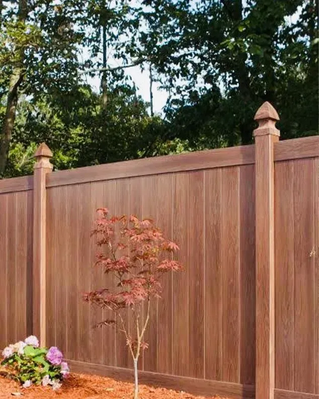 Brown wooden fence with a small tree and pink flowers in front.
