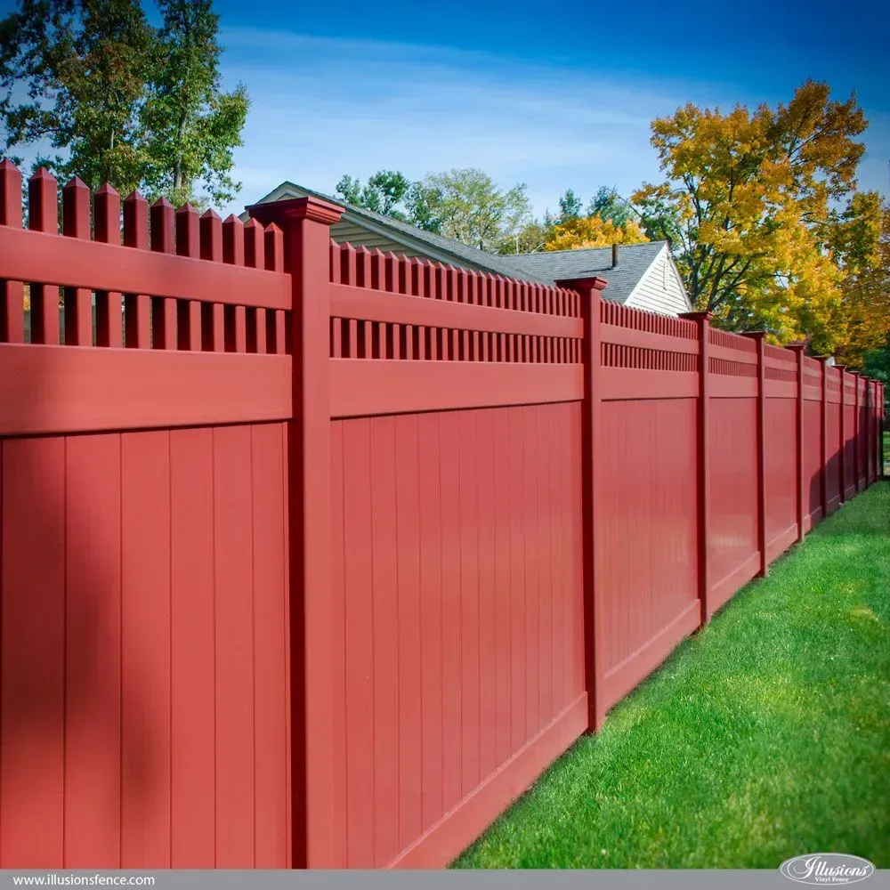 Red wooden fence in a yard with green grass and a house in the background.