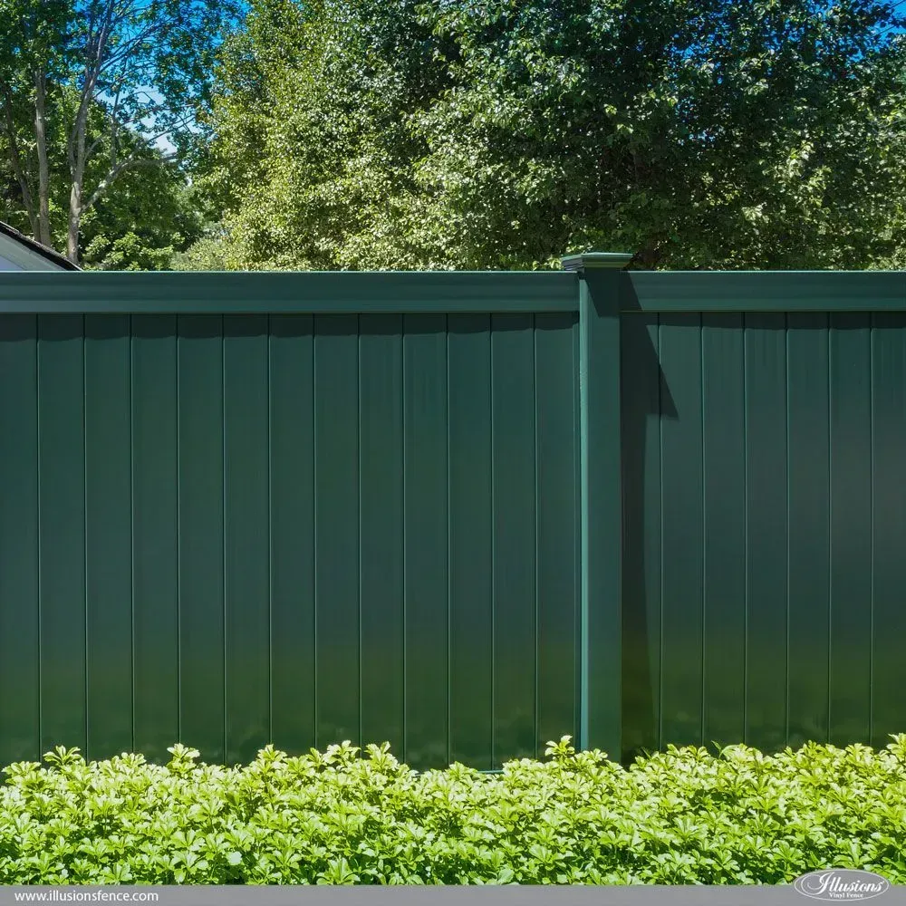 Green vertical panel fence with bushes in front, trees in the background, sunny day.
