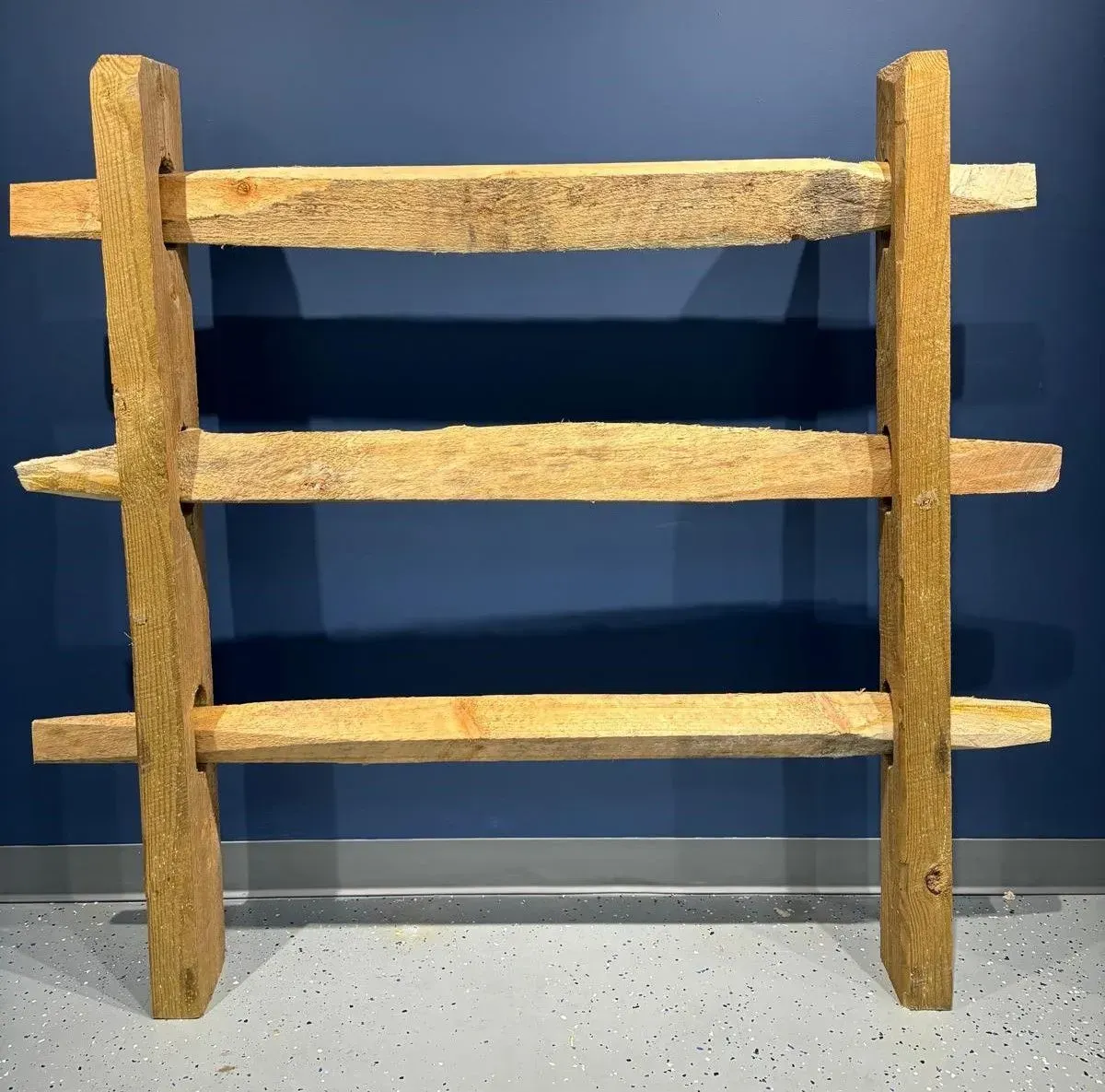 Wooden ladder shelf with three shelves. Against a blue wall.