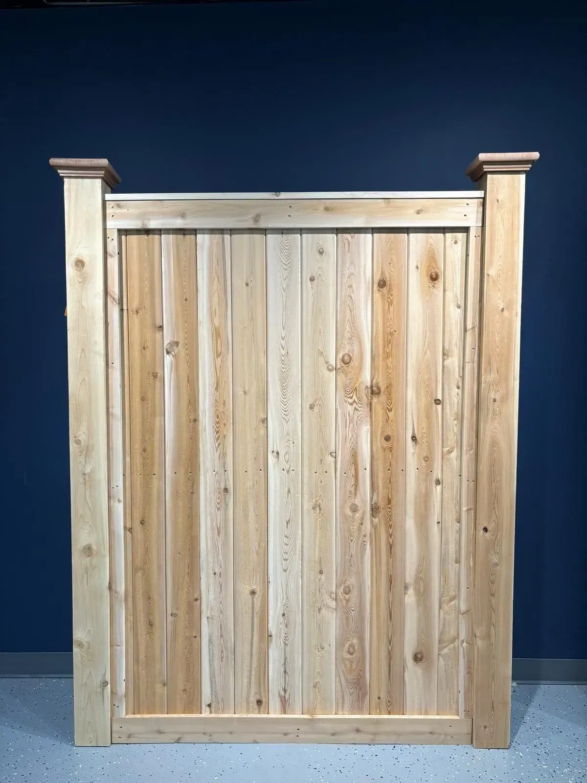 Wooden privacy gate with vertical planks, topped with trim and post caps.