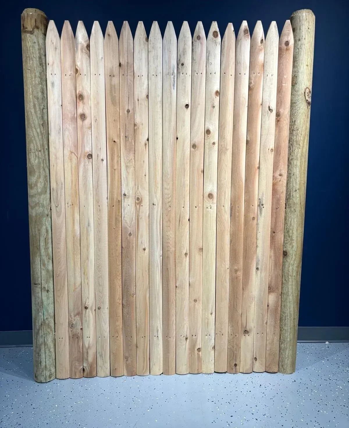 Wooden picket fence section. Vertical light brown planks between two cylindrical posts.
