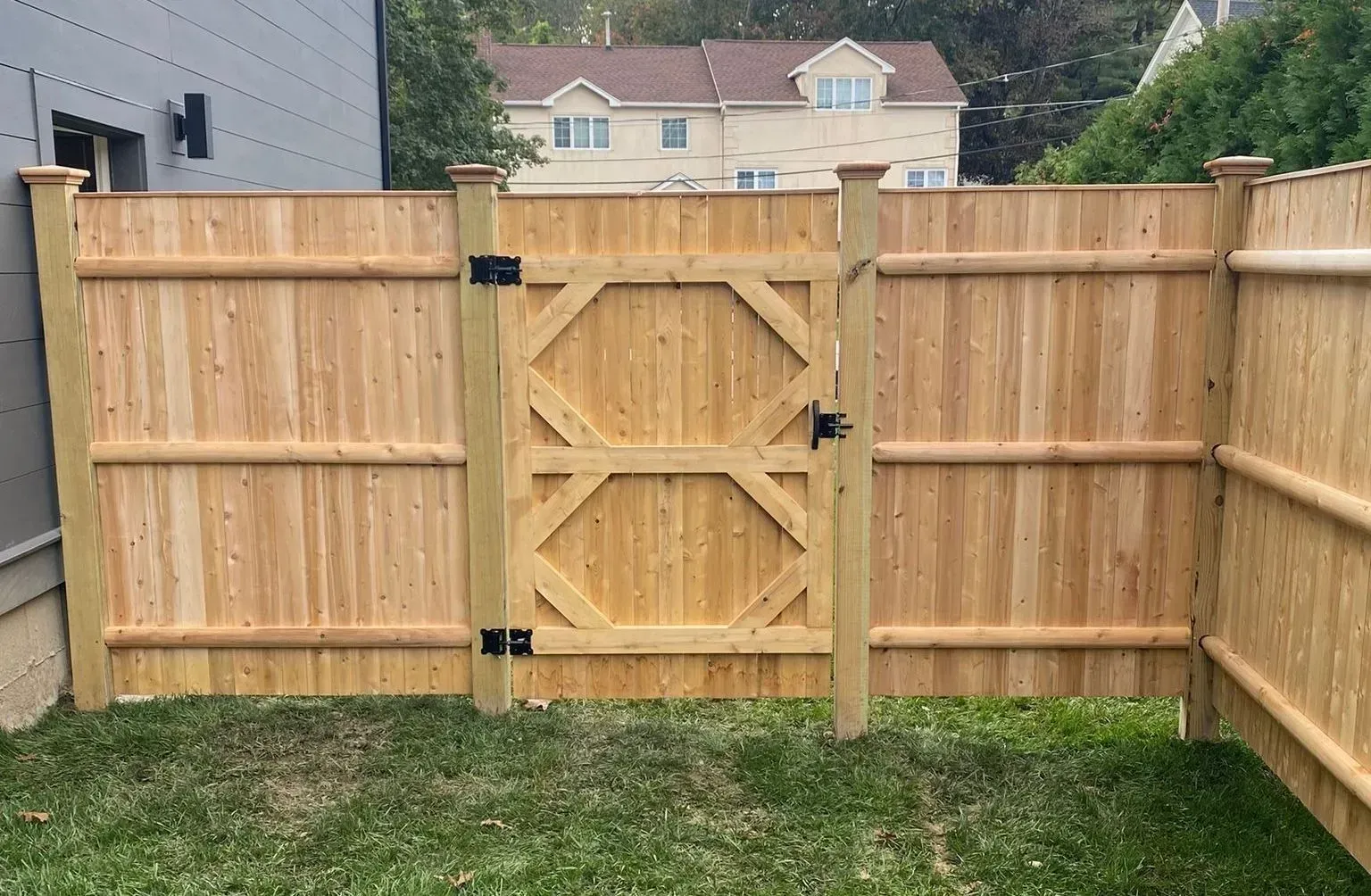 Wooden gate in a cedar fence, opening to a grassy yard.  A house is visible in the background.