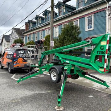 A green aerial lift is parked on the side of the road in front of a building.