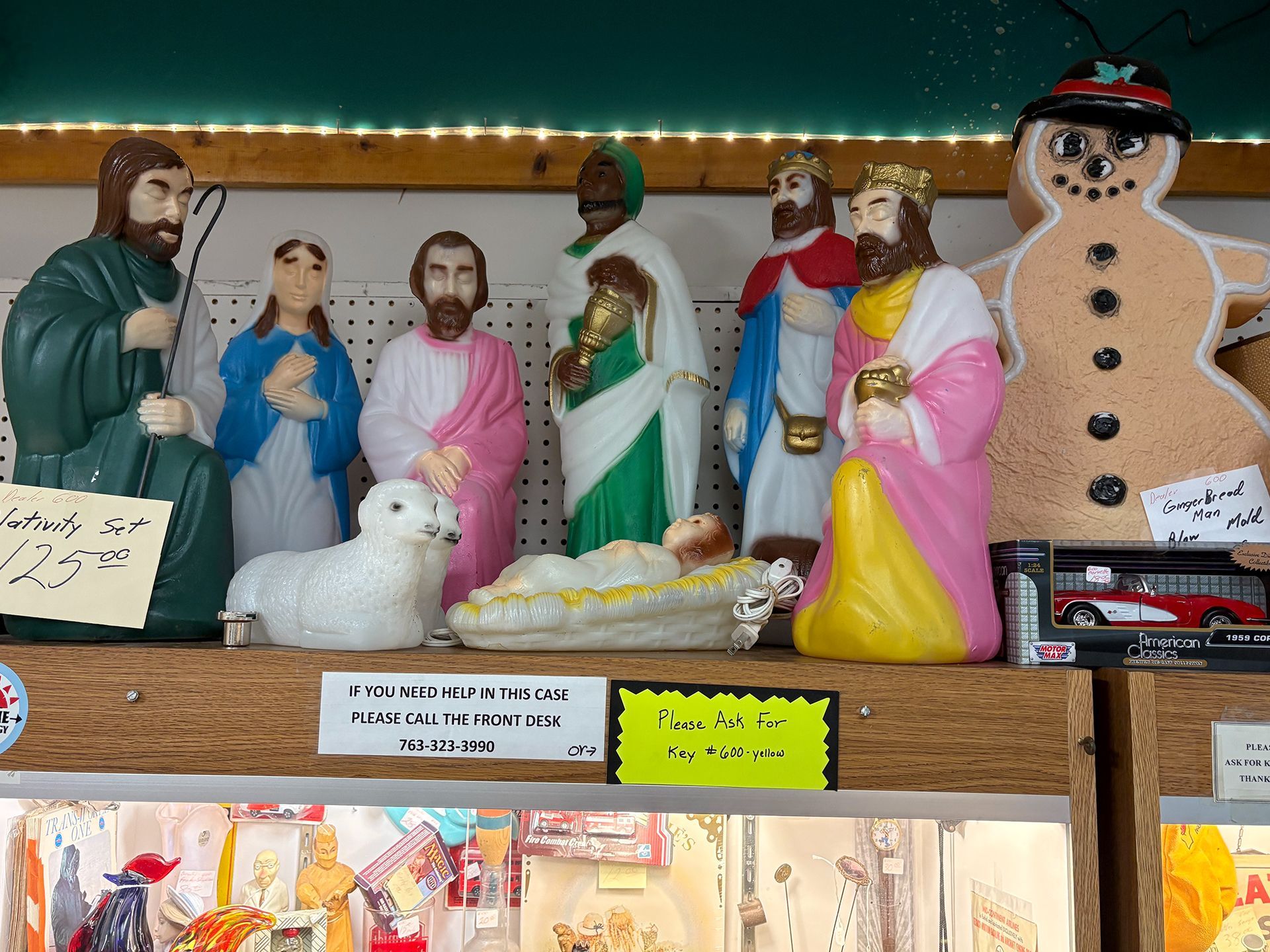 Nativity scene figurines displayed on a shelf: figures of Mary, Joseph, baby Jesus, three wise men, a lamb, and a snowman.