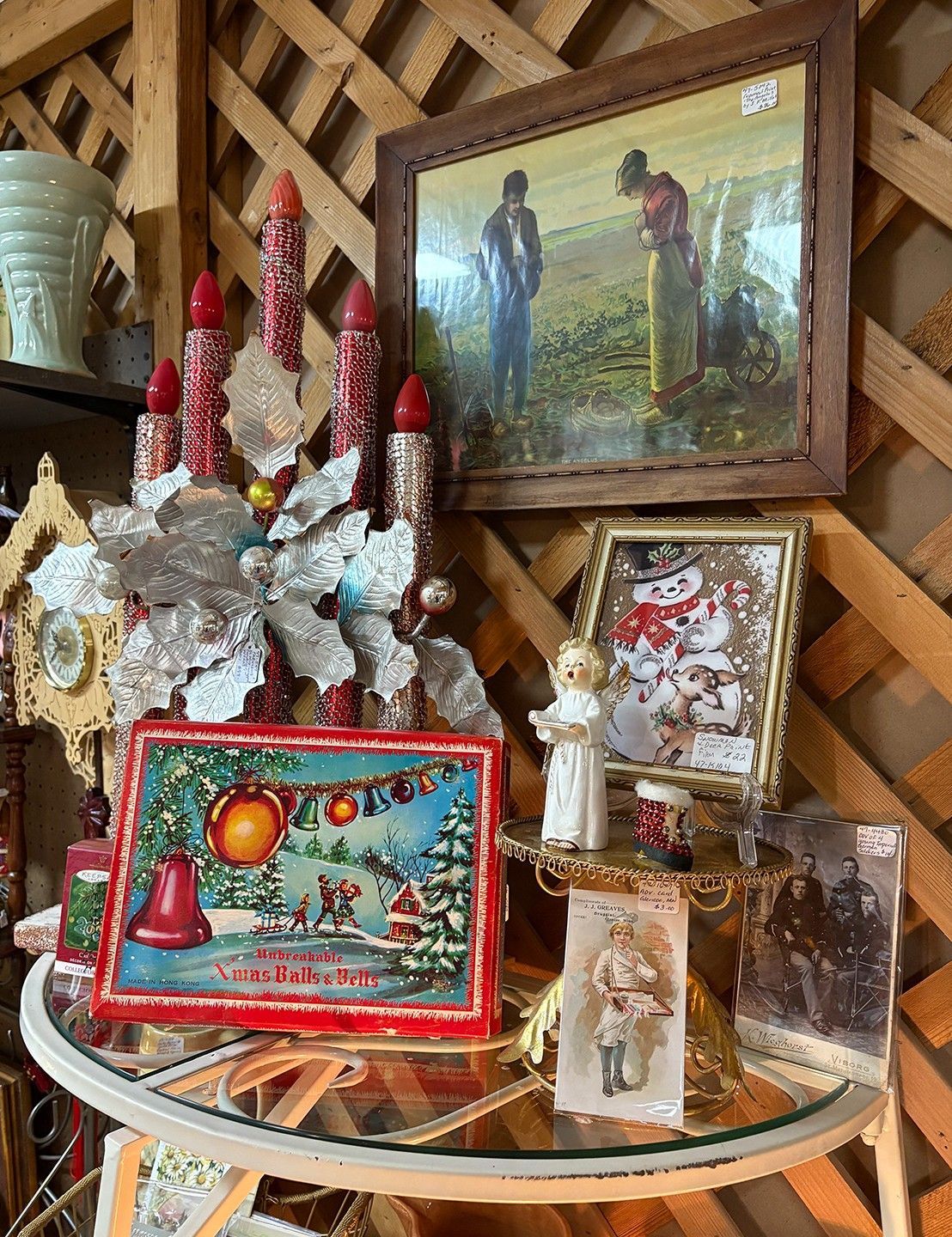A display of vintage Christmas decorations on a glass-topped table. Includes candles, a Santa tin, and framed photos.