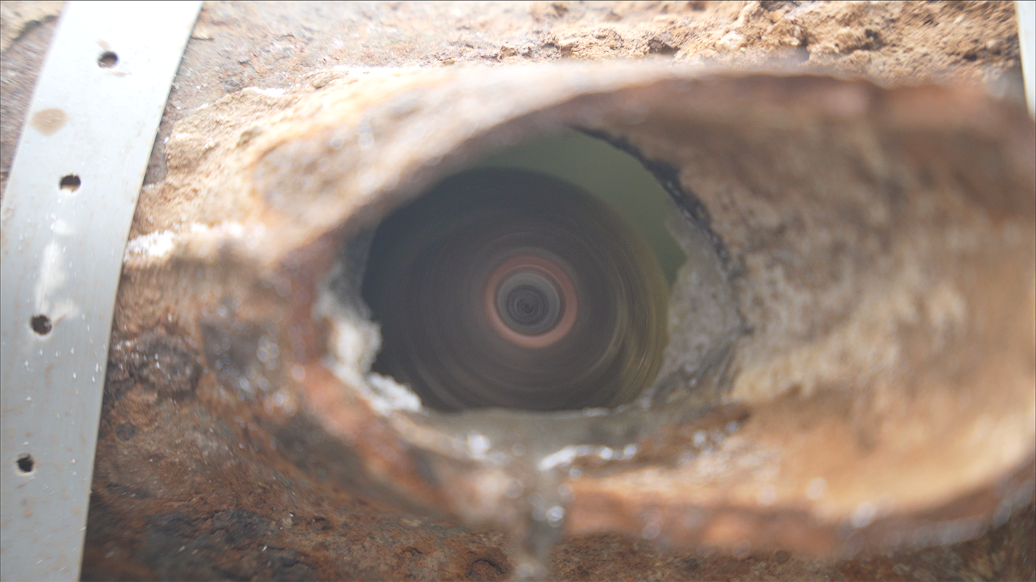 A close up of a hole in a pipe with water coming out of it.