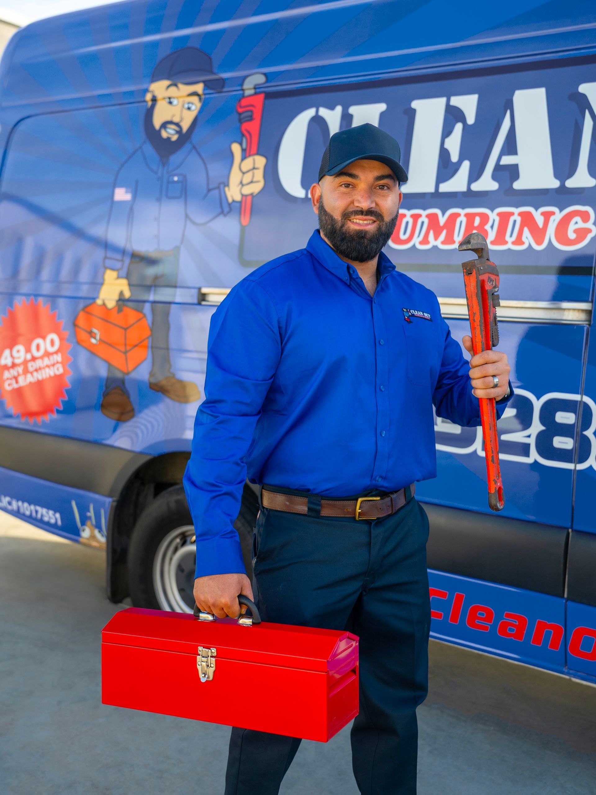 A man standing in front of a clear plumbing van holding a wrench and a toolbox.