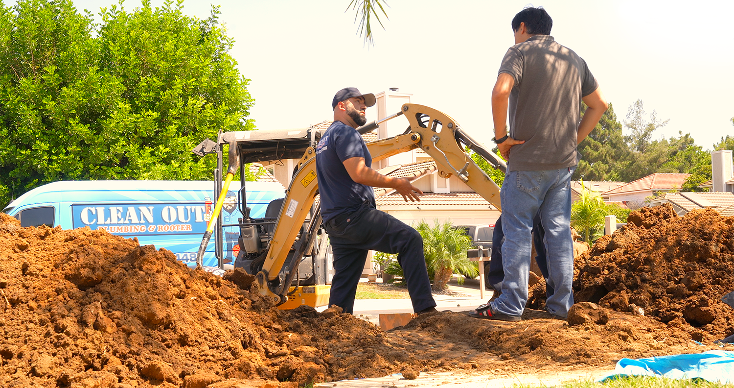Two men are standing in a pile of dirt next to a bulldozer.