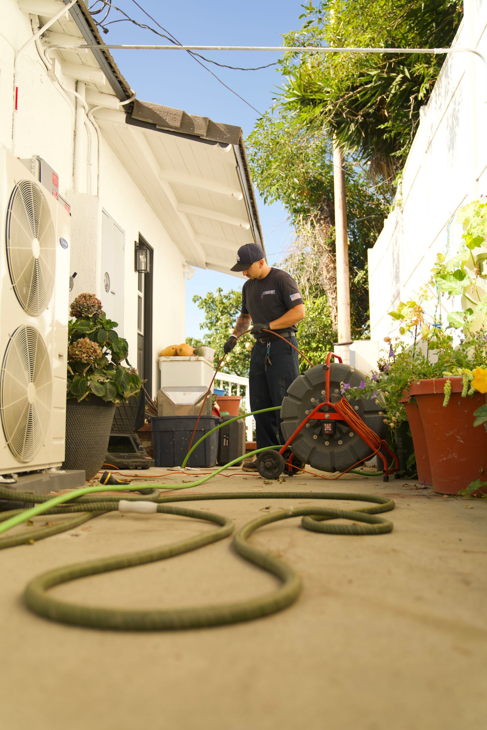 A man is cleaning a drain with a hose in front of a house.