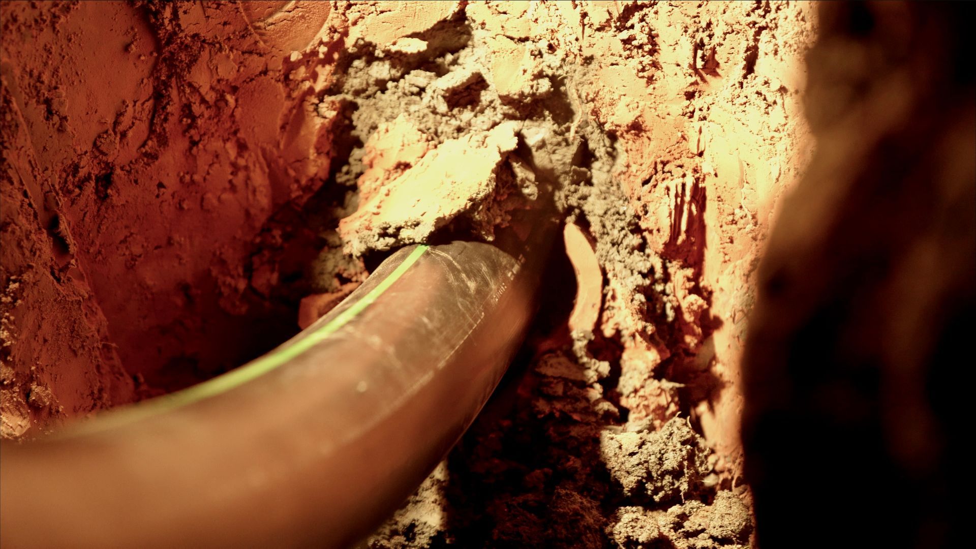 A person is holding a hose in a hole in the ground.