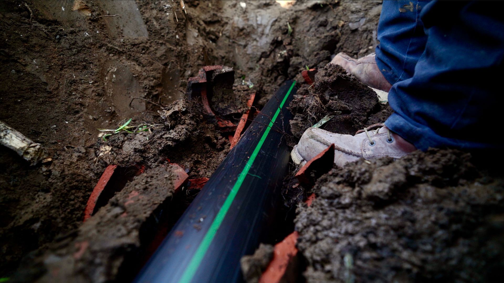 A person is digging a hole in the ground to install a pipe.