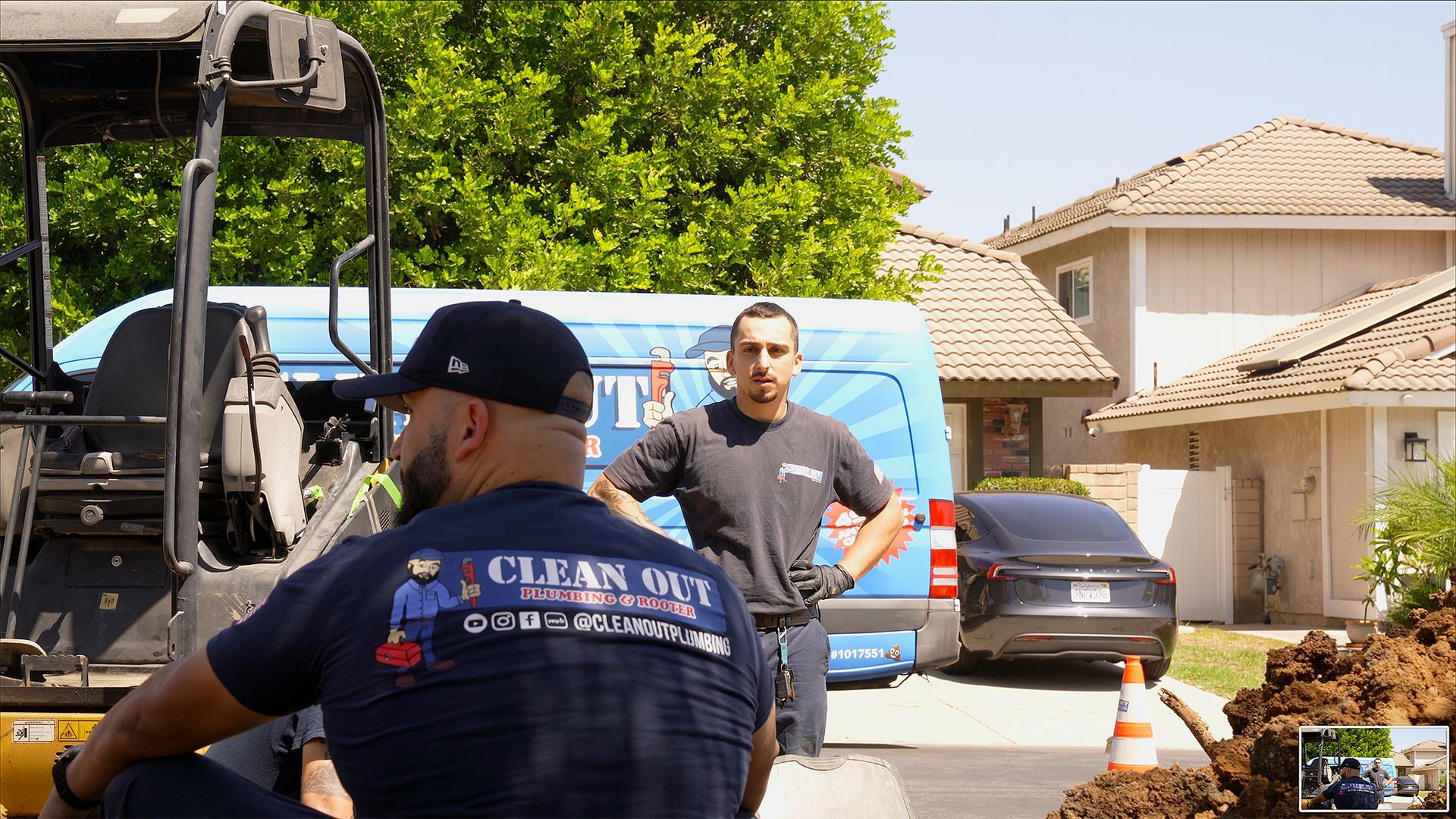Two men are working on a pipe in front of a house.