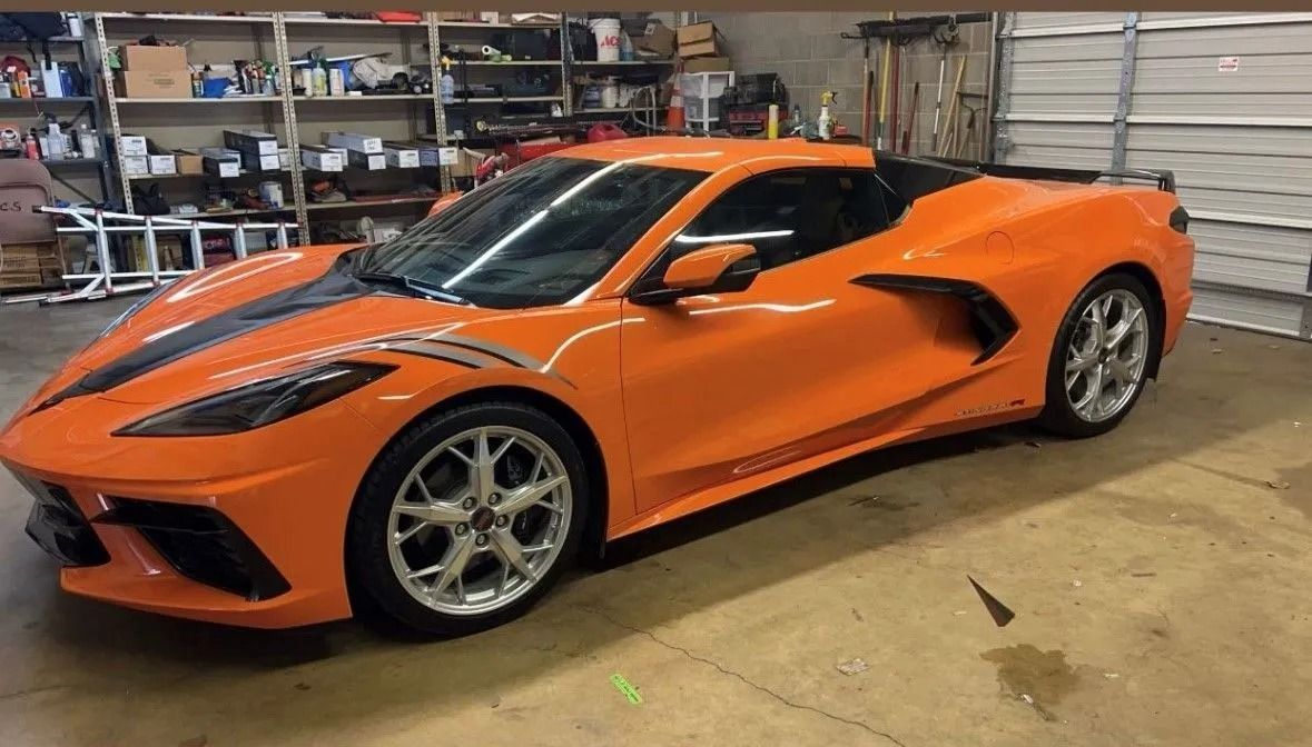 Orange Chevrolet Corvette with black racing stripe parked in a garage.