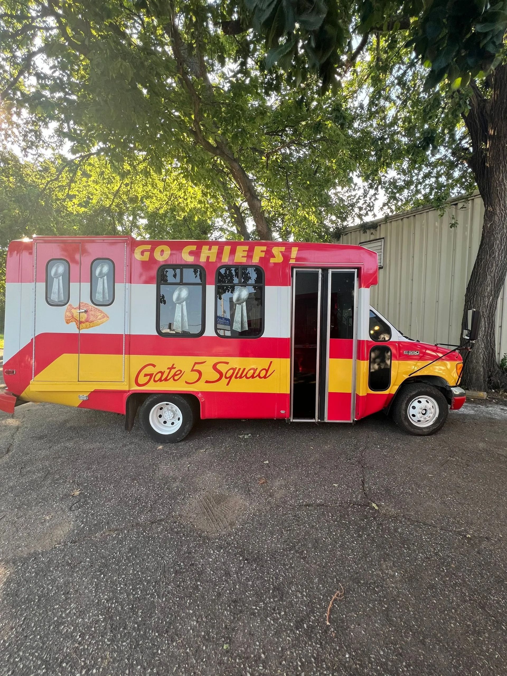 Chiefs-themed bus, red and yellow, with "Go Chiefs!" and "Gate 5 Squad" on the side, parked on gravel.