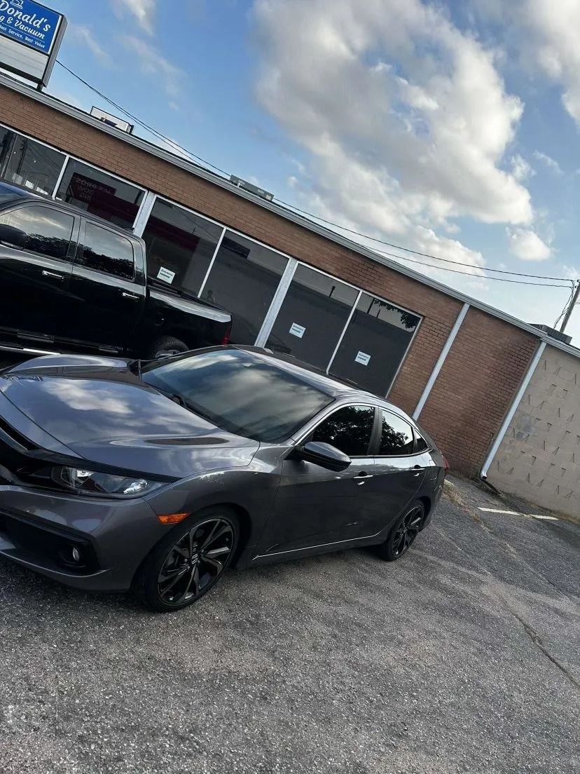 Gray sedan parked in front of a brick building with a cloudy sky overhead.
