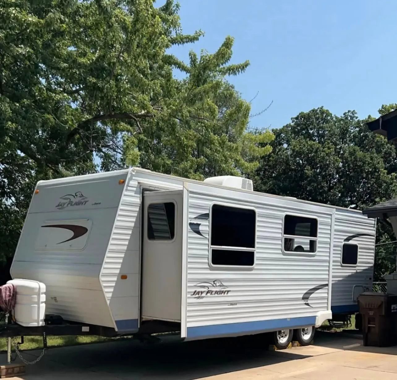 White and blue Jay Feather travel trailer parked outdoors on a sunny day.