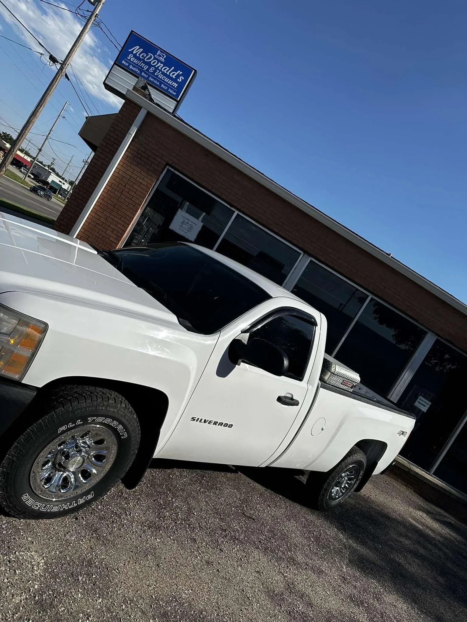 White pickup truck parked outside a brick building with tinted windows on a sunny day.