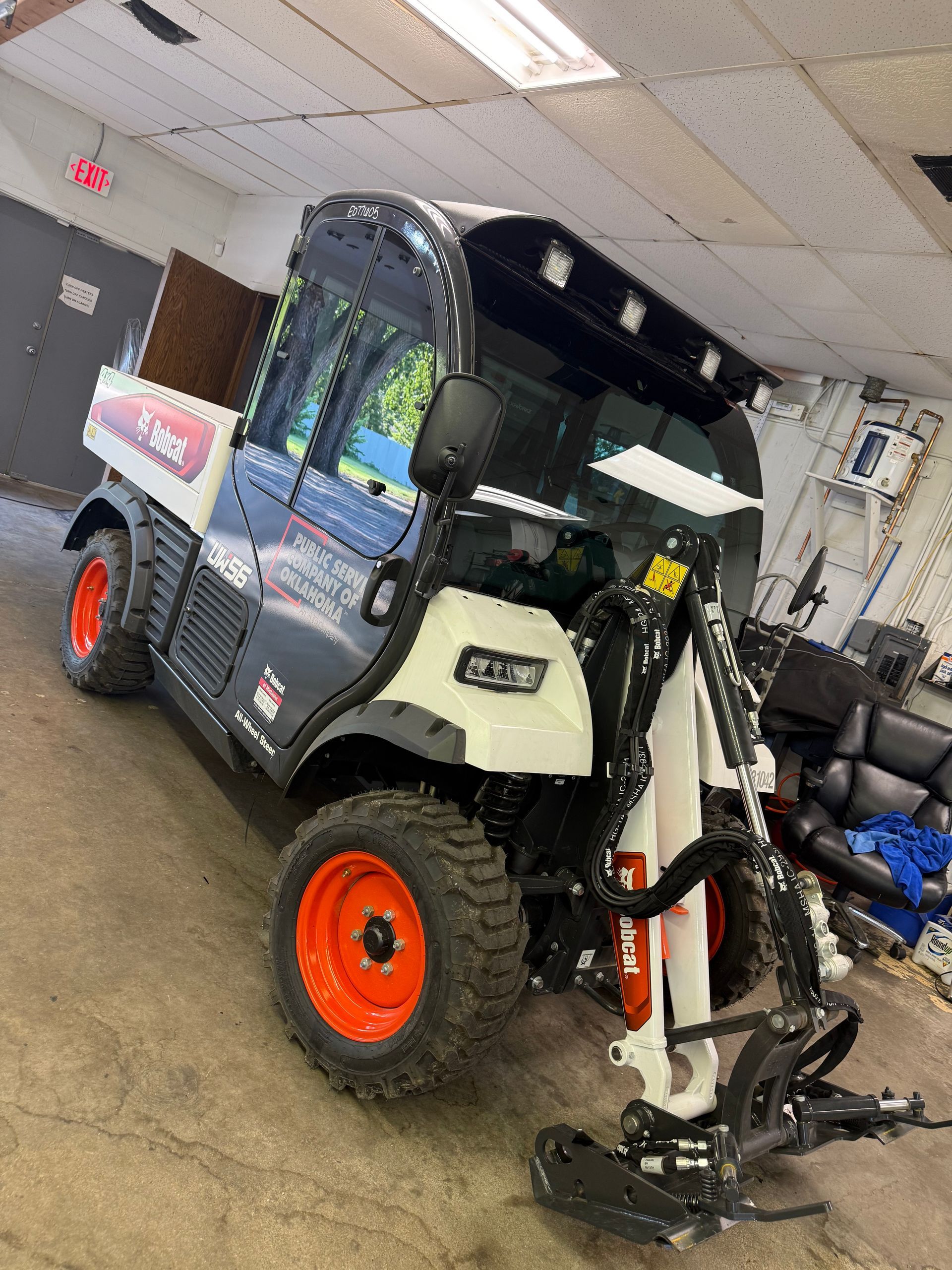 A white and gray Bobcat utility vehicle with an attached front plow, parked inside a garage.