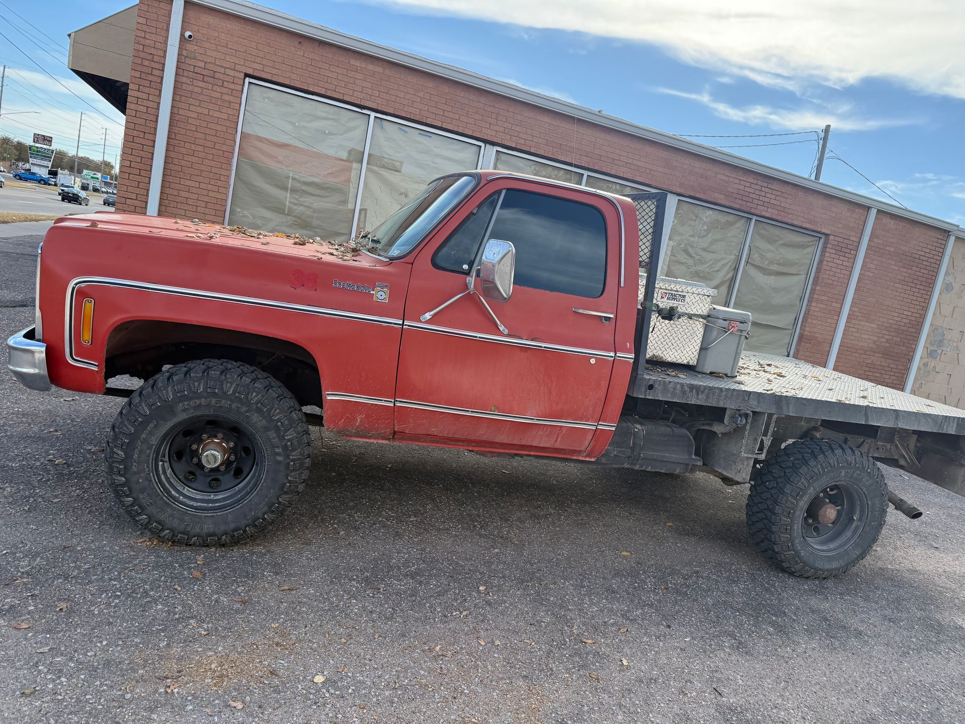 A red flatbed pickup truck parked on gravel in front of a brick building.