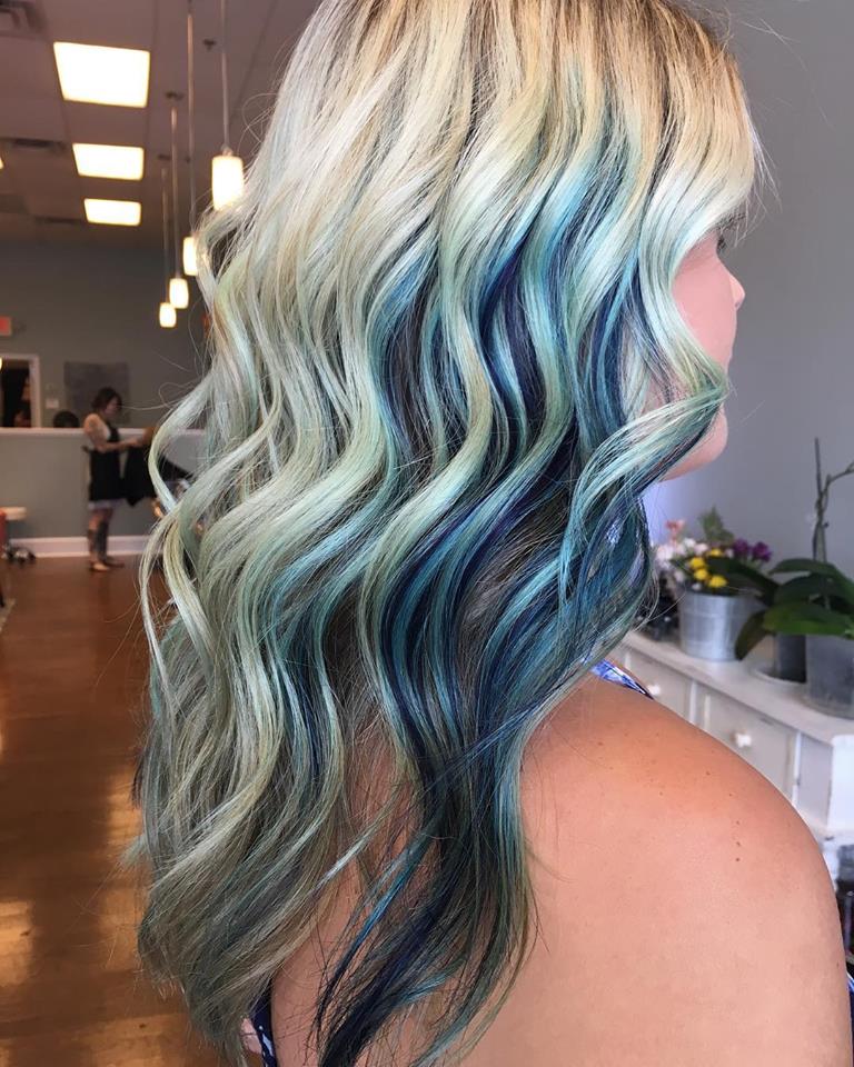 A woman with blonde and blue hair is standing in a salon.