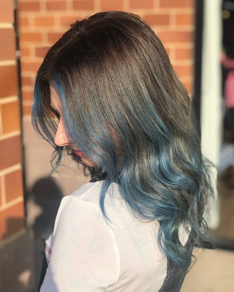 A woman with blue hair is standing in front of a brick wall.