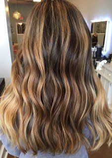 A woman with long wavy brown hair is standing in a salon.