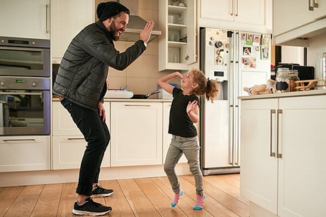 A man and a little girl are dancing in a kitchen.