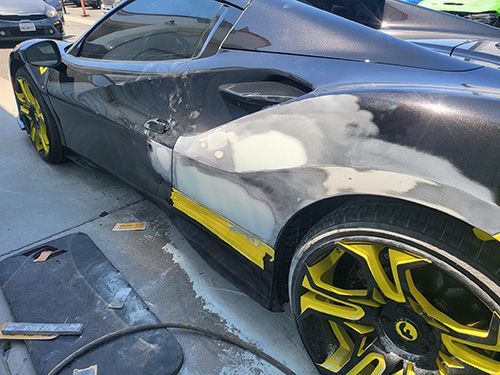 A black and yellow sports car is being repaired in a parking lot.